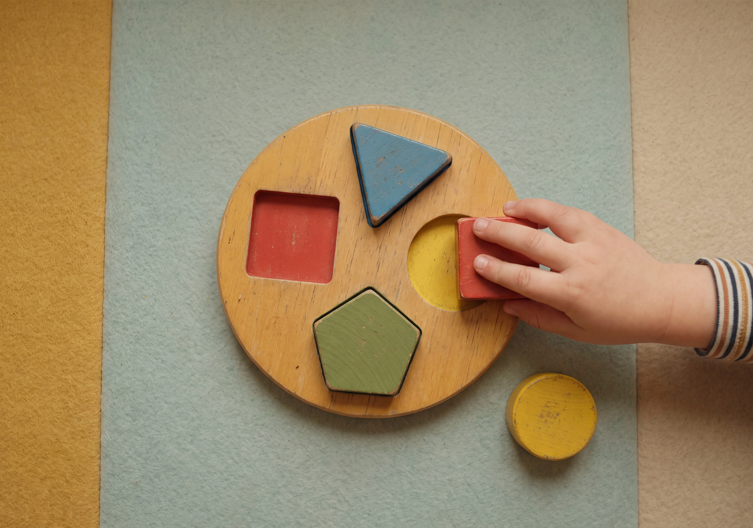 Child fitting wooden shapes into a circular puzzle.