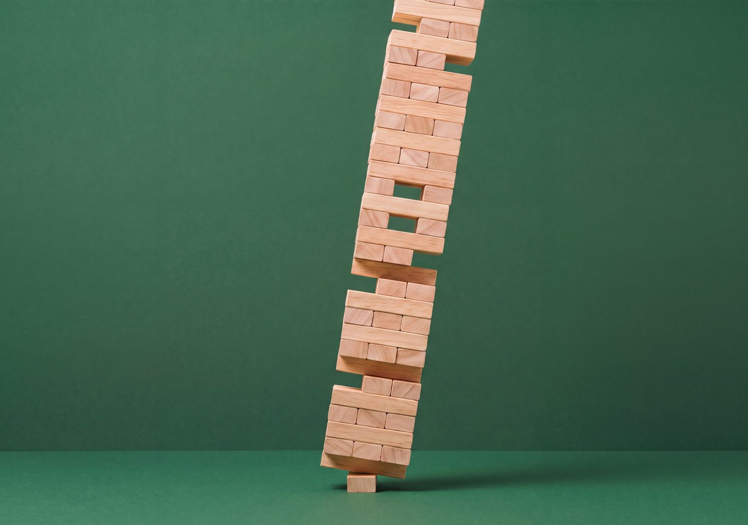 Tall wooden block tower bending against a green background.
